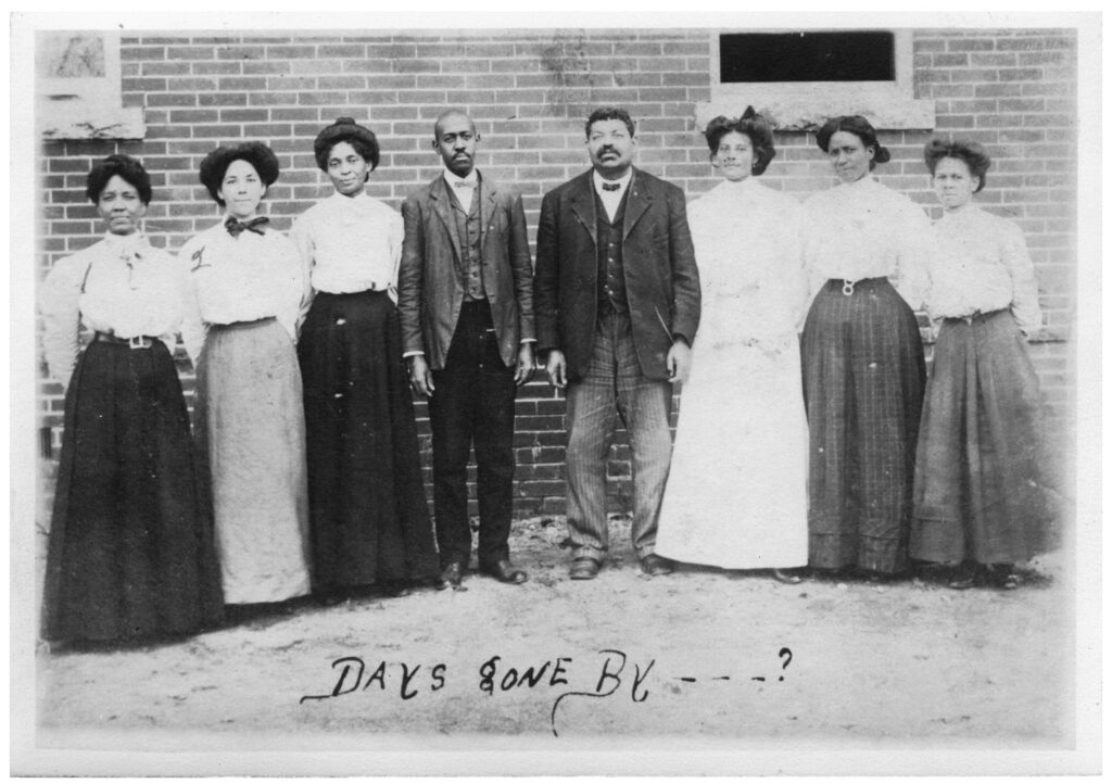 Photograph of the faculty of the Gregory School in 1911. They are standing in a line outside of a building. Handwritten text at the bottom says, "Days gone by...?"