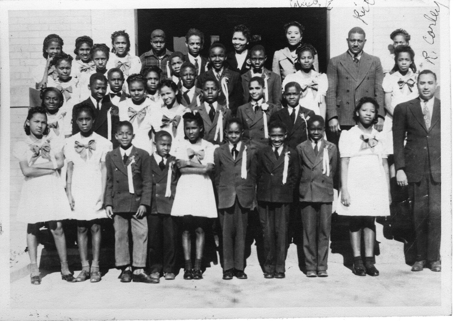 1940s class photo with FR RIce Black and white class photo of African American students and teachers in 1940s period dress standing in front of a brick building.
