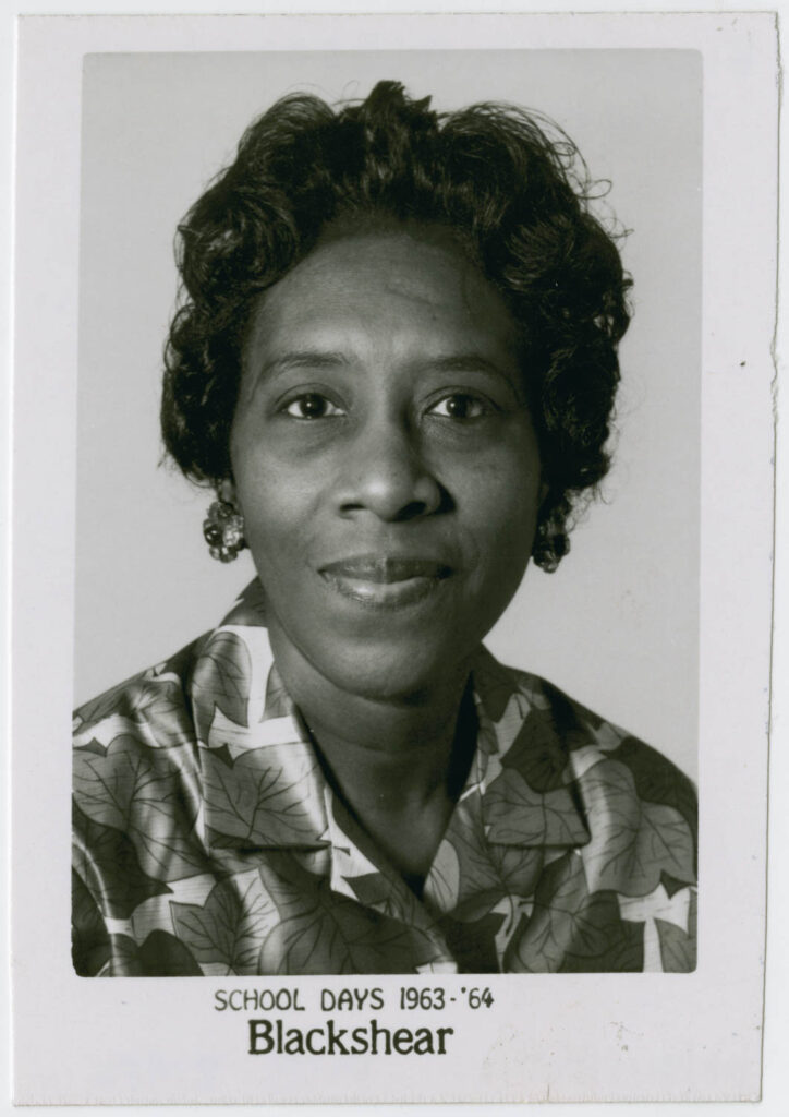 Black and white photo of Algerene Craig, a softly smiling African American woman with short hair in loose curls wearing a silk shirt with a bold leaf pattern.